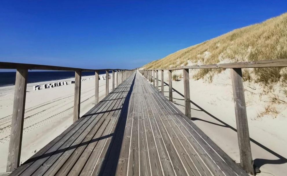 Ein Holzsteg entlang des strahlend weißen Sandstrandes in Sylt.
