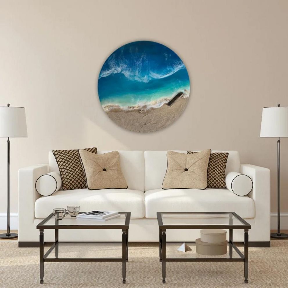 Ein kunstvolles rundes Bild in Meersicht gemalt oberhalb eines weißen prächtigen Sofas an der Wand hängend.