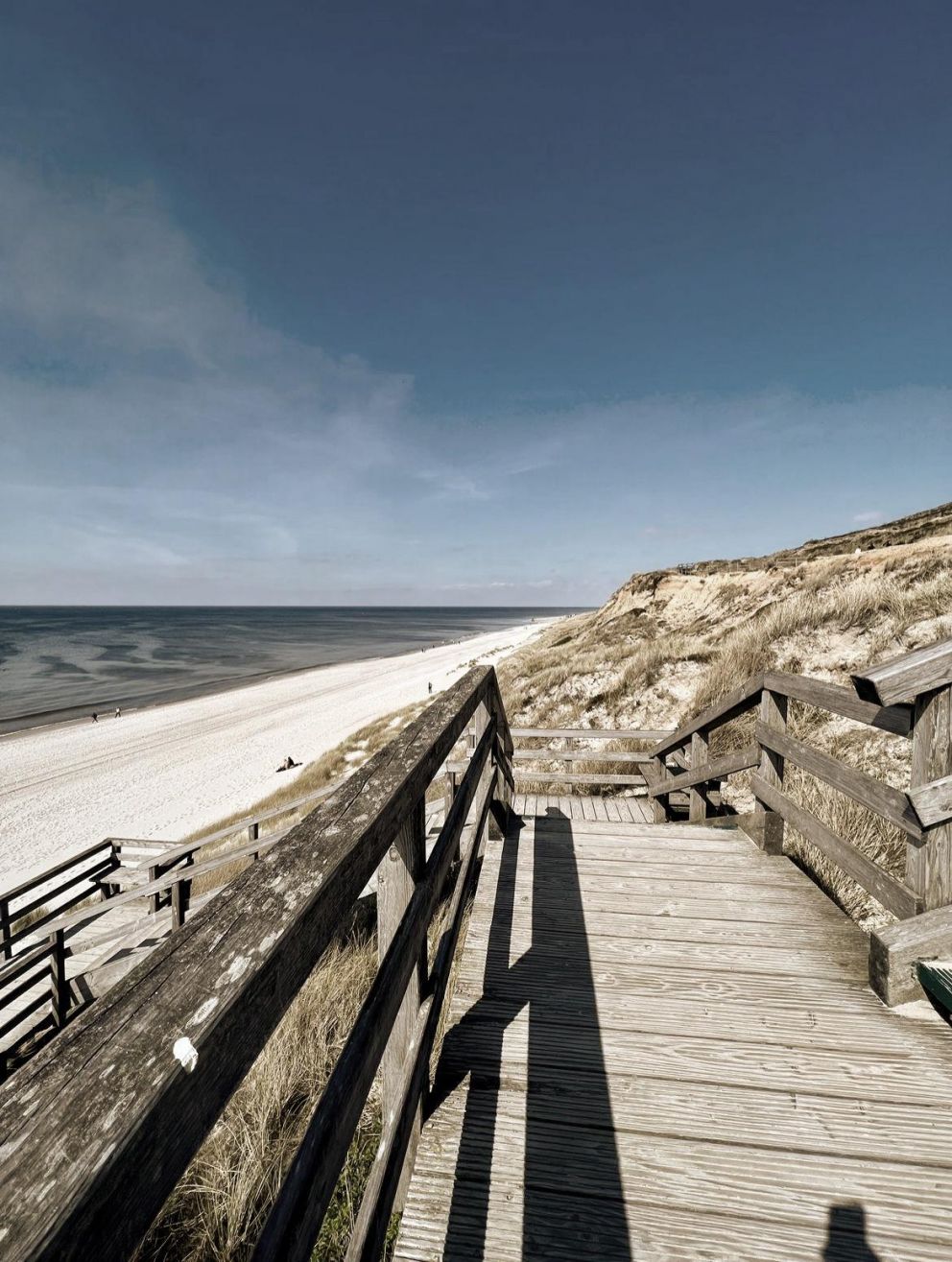 Eine Holztreppe führt zu dem langen weißen Sandstrand in Sylt.